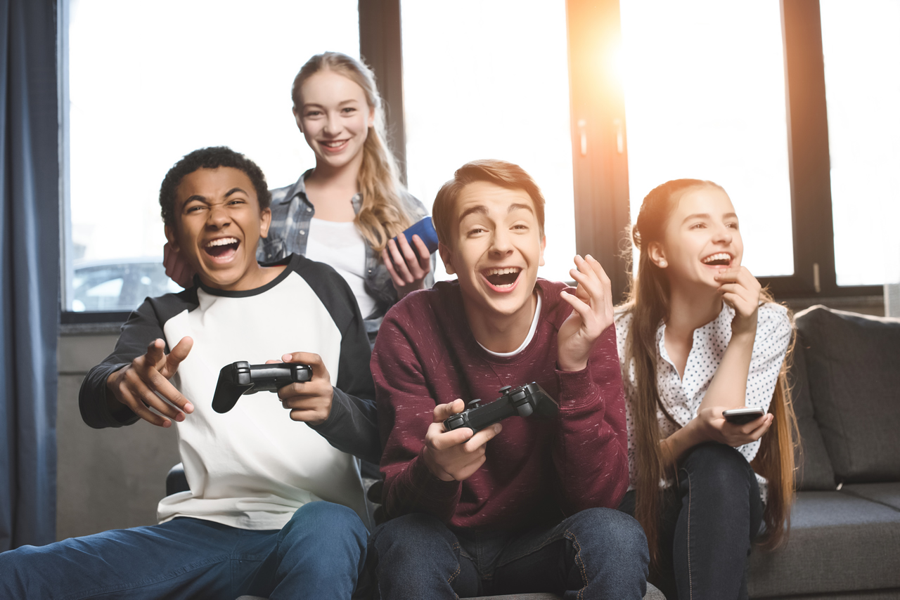 four teens playing video games smiling